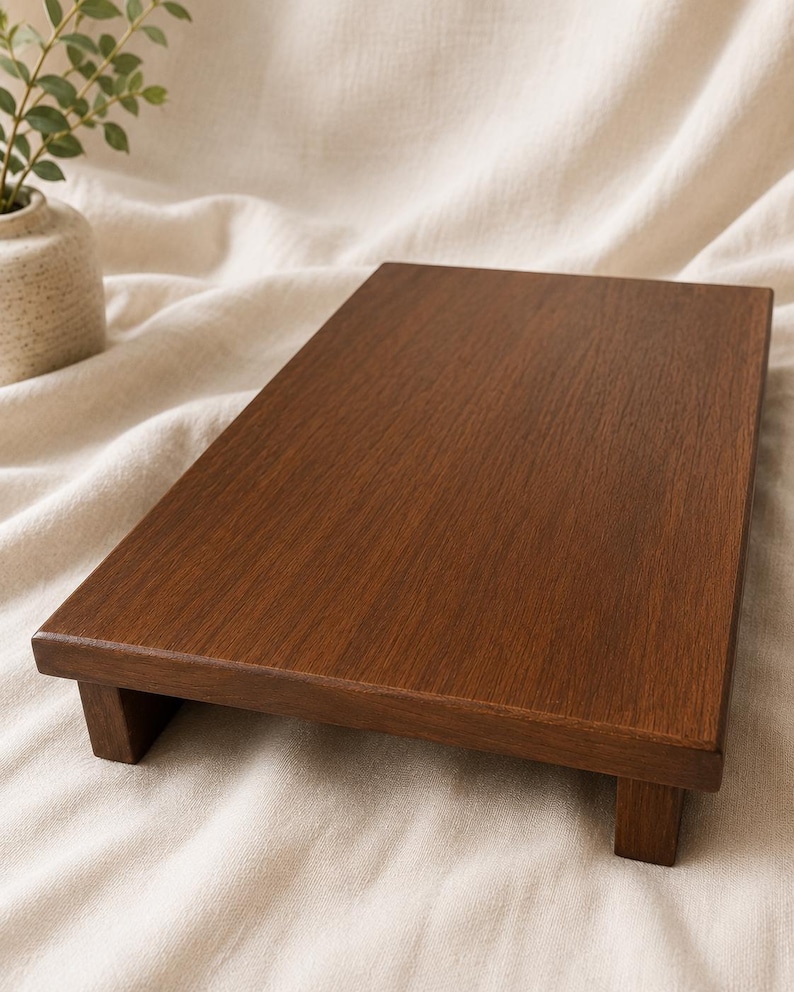 May include: A dark brown wooden serving tray with a rectangular shape, raised edges, and short legs. The tray is made of a rich, warm-toned wood and sits on a cream-coloured fabric surface. The tray is suitable for serving food or displaying decorative items.
