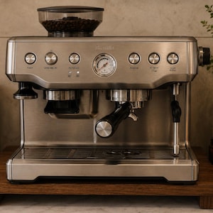 May include: Stainless steel espresso machine with an integrated grinder. The machine features several buttons and a pressure gauge. A clear container on top holds coffee beans. The machine is on a wooden base.