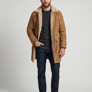 May include: A tan suede coat with a cream shearling collar and lining. The coat features a button closure, two front pockets, and sleeve belt details. The person is wearing a dark grey jumper, dark blue jeans, and brown leather boots.