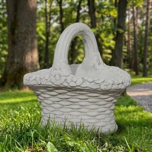 May include: A light gray concrete basket planter featuring a textured woven pattern on the exterior body and a decorative floral band around the rim, topped with a high arched handle that has a smooth, curved design.