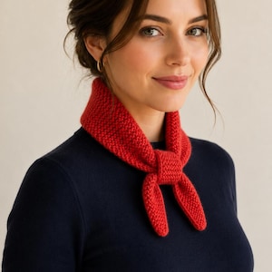 May include: A bright red knitted neckerchief featuring a textured garter stitch pattern, tied in a simple knot at the front. The accessory is worn over a plain, dark navy blue long-sleeved sweater with a round neckline and a fitted silhouette.