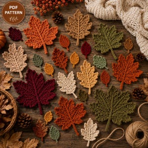 Könnte beinhalten: Eine Sammlung gehäkelter Herbstblätter in verschiedenen Formen und Größen in den Farben Orange, Rot, Gelb, Beige und Grün. Die Blätter sind auf einer Holzoberfläche zusammen mit kleinen Tannenzapfen und einem Garnknäuel angeordnet.
