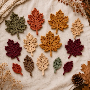 Può includere: Una collezione di foglie all'uncinetto in vari colori autunnali, tra cui verde oliva, arancione bruciato, giallo senape, beige, marrone scuro e bordeaux intenso. Le foglie presentano motivi a punto intricati e steli su un tessuto neutro.