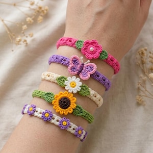 May include: A collection of colorful crochet bracelets. The bracelets feature floral and butterfly designs in shades of pink, purple, yellow, green, and white. Each bracelet is adorned with intricate details, including a sunflower, daisy, and small flowers.