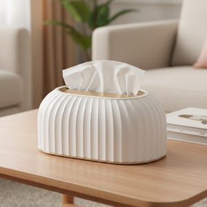 Op de afbeelding: Een witte tissuebox met een geribbeld ontwerp en gouden rand, met witte tissues. De box staat op een lichtbruine houten tafel, met een neutraal getinte woonkamer op de achtergrond. De tissuebox heeft een moderne, minimalistische uitstraling.