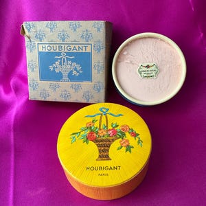 May include: A Houbigant Paris powder set including a square cardboard box with a blue floral basket print, a round yellow container with a floral basket illustration, and an open round container revealing light pink powder and a small label.