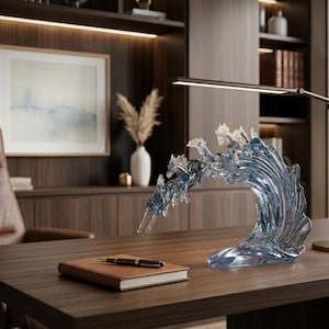 Peut inclure: Une sculpture en verre bleu clair représentant des chevaux sautant à travers une vague. L'objet décoratif est posé sur un bureau en bois foncé avec un cahier et un stylo. L'arrière-plan comprend un tableau encadré et une lampe de bureau.