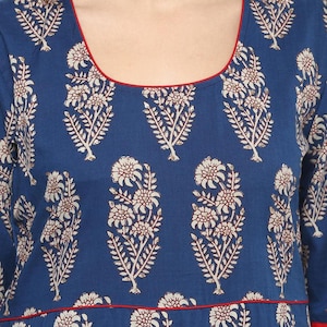 May include: A blue garment with a floral pattern. The design features white and brown floral motifs against a dark blue background. The neckline and hemline are trimmed with a thin red border. The fabric appears to be a soft, flowing material.