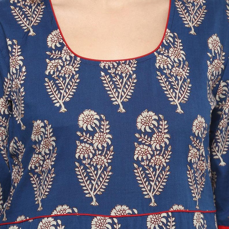 May include: A blue garment with a floral pattern. The design features white and brown floral motifs against a dark blue background. The neckline and hemline are trimmed with a thin red border. The fabric appears to be a soft, flowing material.