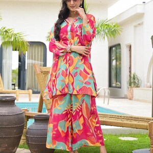 Könnte beinhalten: Ein zweiteiliges Set bestehend aus einem langärmeligen Hemd mit Knopfleiste und einer weiten Hose, mit einem lebendigen abstrakten Blumenmuster in Pink, Türkis, Orange und Gelb, mit klassischem Kragen und lockerer Passform.