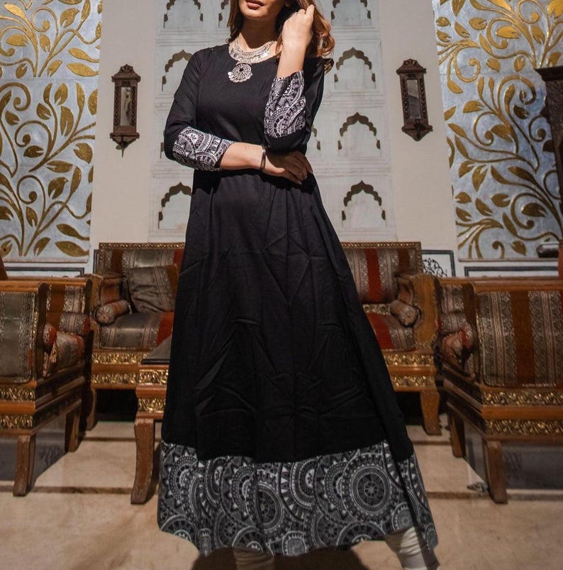 May include: A black long-sleeve dress with a flared skirt and a decorative hemline. The sleeves feature a white and black patterned design. The dress is accessorized with a silver necklace. The dress is suitable for casual or formal occasions.