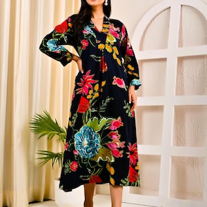 Peut inclure: Longue robe bleu foncé ornée d'un motif floral vibrant rouge, rose, jaune et bleu. La robe a des manches longues et un col en V. Le motif floral est concentré sur la moitié inférieure.