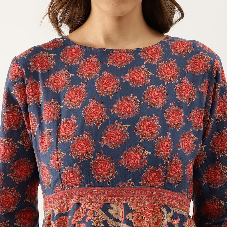 Puede incluir: Vestido de manga larga con fondo azul marino y un estampado repetido de rosas rojas. El vestido tiene un corpi&ntilde;o ajustado y un estampado floral rojo y beige en la cintura y la falda.
