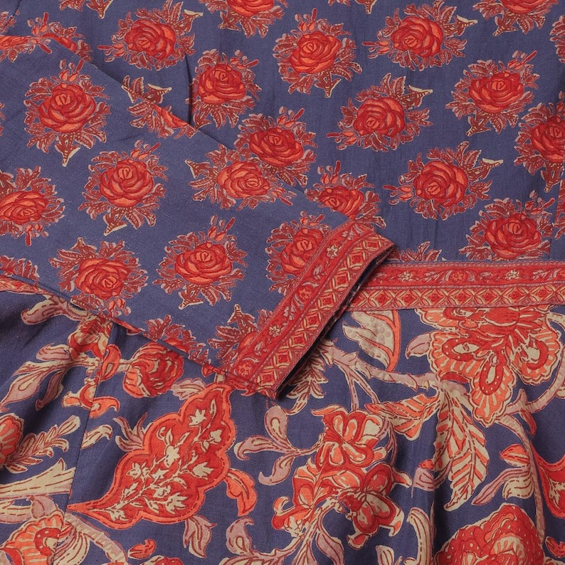 Puede incluir: Primer plano de una tela azul con un patr&oacute;n repetido de rosas rojas. La tela tambi&eacute;n presenta un dise&ntilde;o floral en rojo y crema. El pu&ntilde;o de la manga y el escote est&aacute;n ribeteados con un borde geom&eacute;trico rojo.