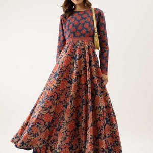Puede incluir: Un vestido de manga larga con un estampado floral en rojo y beige sobre un fondo azul marino. El vestido tiene un cuello redondo y una cintura entallada. La falda se ensancha, creando una silueta fluida. Un peque&ntilde;o bolso de color claro cuelga del hombro.