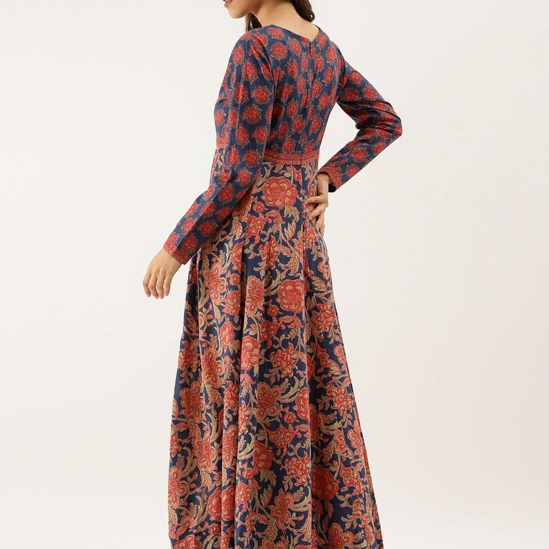Puede incluir: Un vestido largo de manga larga con un estampado floral en tonos azul marino, rojo y dorado. El vestido presenta un escote en V y un corpi&ntilde;o ajustado que fluye hacia una falda acampanada. El estampado floral es consistente en todo el vestido.