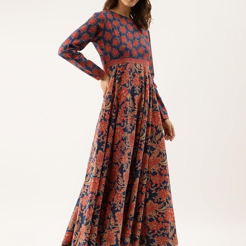 Puede incluir: Un vestido largo de manga larga con un estampado floral en tonos azul marino, rojo y beige. El vestido tiene un cuello redondo y un corpi&ntilde;o ajustado que fluye hacia una falda amplia. La tela parece ligera y adecuada para climas c&aacute;lidos.