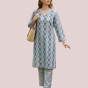Könnte beinhalten: Eine langärmelige Tunika mit blau-weißem Rauten-Ikat-Muster und V-Ausschnitt, kombiniert mit einer passenden gerade geschnittenen Hose mit blau-weißem Zickzackmuster sowie einer beigen, geflochtenen Stroh-Umhängetasche mit braunen Riemen.