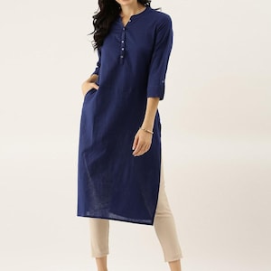 Könnte beinhalten: Ein marineblaues Tunika-Shirt mit Stehkragen und Dreiviertelärmeln. Das Shirt hat eine Knopfleiste vorne und zwei Taschen. Das Model trägt eine beige Hose. Die Tunika ist etwa 102 cm lang.