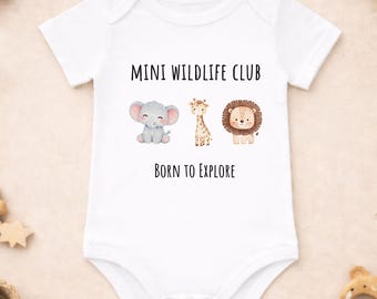 Puede incluir: Body de bebé blanco con el texto "MINI WILDLIFE CLUB" y "BORN TO EXPLORE". El body presenta ilustraciones de un elefante, una jirafa y un león. El body es de manga corta.