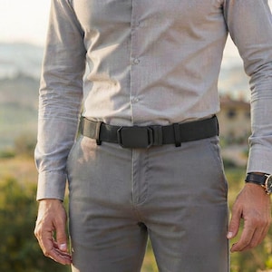 May include: A light gray long-sleeved button-down shirt tucked into gray trousers, secured with a black tactical-style belt featuring a rectangular matte black buckle. The belt is made of a woven fabric material and sits at the waistline.
