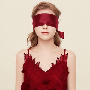 May include: A deep red satin blindfold tied at the side, paired with a matching deep red sleeveless top featuring a V-neckline and intricate leaf-shaped embroidery along the edges. The set is monochromatic, showcasing a consistent dark red hue.