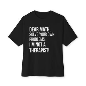 May include: Black t-shirt with white text: "DEAR MATH, SOLVE YOUR OWN PROBLEMS. I'M NOT A THERAPIST!" The tee has short sleeves and a crew neck. The text is centered on the front of the garment.