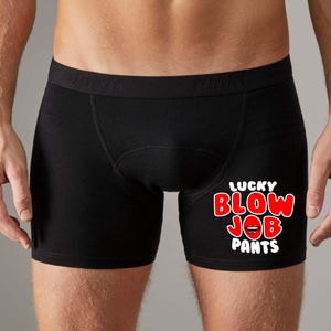 May include: Black boxer shorts with the text "LUCKY BLOW JOB PANTS" in red and white. The text includes a graphic of red lips. The underwear is made of a soft material.