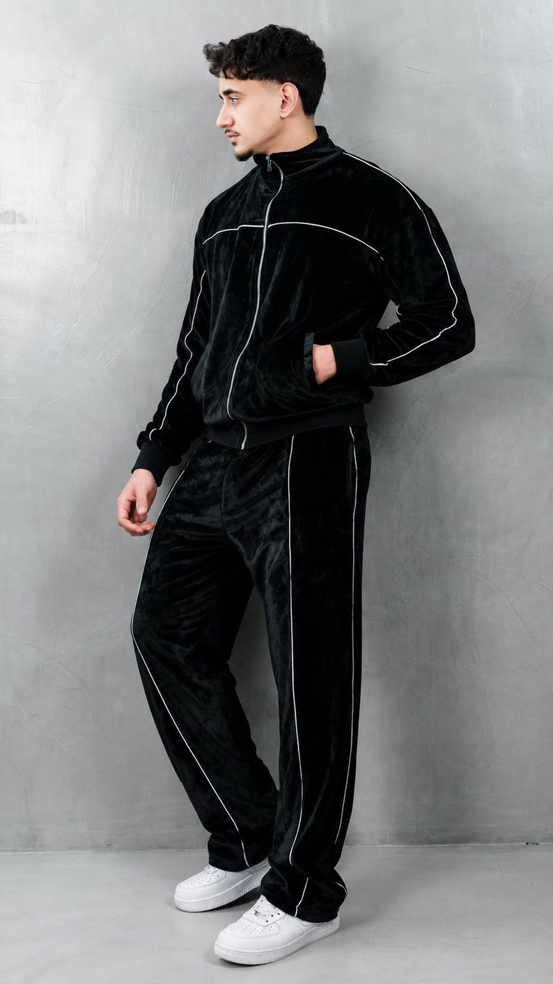 K&ouml;nnte beinhalten: Schwarzer Velours-Trainingsanzug mit wei&szlig;er Paspelierung. Die Jacke hat einen Rei&szlig;verschluss und Taschen, und die Hose hat einen geraden Beinverlauf. Das Outfit wird mit wei&szlig;en Turnschuhen getragen. Dieser bequeme Trainingsanzug ist f&uuml;r Freizeitkleidung geeignet.