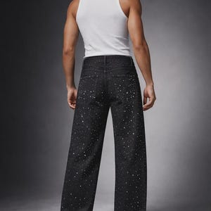 Puede incluir: Vaqueros negros de mezclilla con corte de pierna ancha, con un patr&oacute;n blanco moteado. El modelo lleva una camiseta sin mangas blanca y zapatillas blancas. Los vaqueros tienen un dise&ntilde;o cl&aacute;sico de cinco bolsillos.