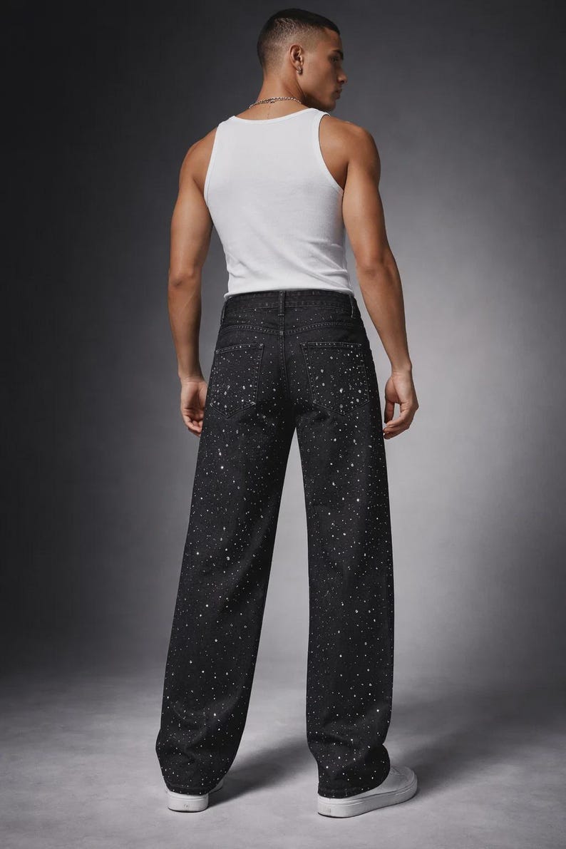 Puede incluir: Vaqueros negros de mezclilla con corte de pierna ancha, con un patr&oacute;n blanco moteado. El modelo lleva una camiseta sin mangas blanca y zapatillas blancas. Los vaqueros tienen un dise&ntilde;o cl&aacute;sico de cinco bolsillos.