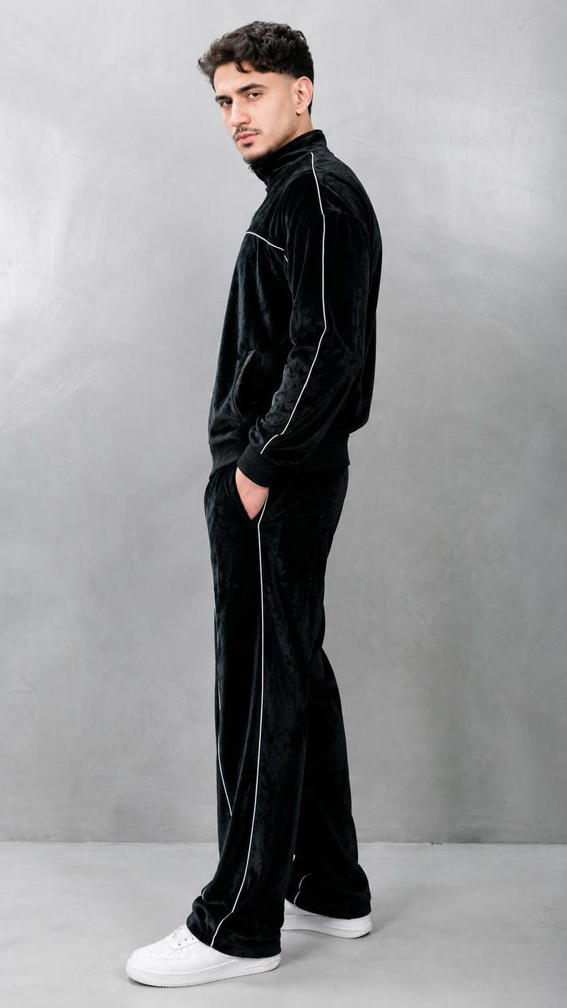 K&ouml;nnte beinhalten: Ein schwarzer Velours-Trainingsanzug mit wei&szlig;en Paspeln. Der Anzug besteht aus einer Jacke mit Rei&szlig;verschluss und einer passenden Hose. Die Person tr&auml;gt wei&szlig;e Turnschuhe. Das Outfit ist ein l&auml;ssiger, bequemer Stil.