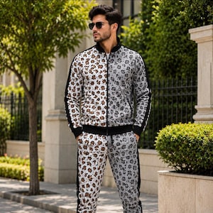 Puede incluir: Un conjunto de chándal de dos piezas con un diseño bicolor, que presenta un estampado de leopardo marrón y blanco en el lado izquierdo y un estampado de leopardo gris y blanco en el lado derecho. La chaqueta tiene cuello alto, puños y bandas negros.
