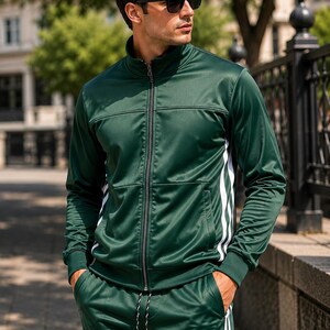 May include: A dark green track jacket and matching track pants set featuring a high collar, a full-length front zipper, and two vertical white stripes running down the outer sides of the sleeves and legs. The fabric has a smooth, sheen finish.