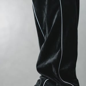 K&ouml;nnte beinhalten: Schwarze Samt-Trainingshose mit wei&szlig;em Paspeldetail. Die Hose wird mit wei&szlig;en Ledersneakern kombiniert. Die Sneaker haben das Wort "AIR" auf der Seite. Die Hose ist leicht zerknittert.