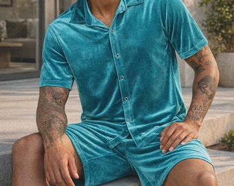 May include: Teal velvet pajama set. The set includes a short-sleeved button-down shirt and matching shorts. The shirt has a classic collar and button closure. The shorts have a relaxed fit. The fabric has a soft, luxurious appearance.