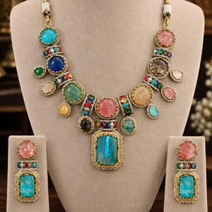 May include: A gold-toned statement necklace and matching earrings set featuring an array of multi-coloured cabochon stones in shades of blue, pink, green, and yellow, accented with small clear crystals and intricate metalwork borders.