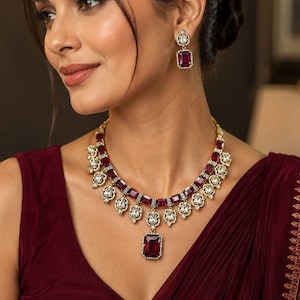 May include: A gold-toned necklace and matching drop earrings set featuring rectangular deep red stones surrounded by small clear white crystals. The necklace has a central pendant and a series of smaller rectangular red stones along the chain.