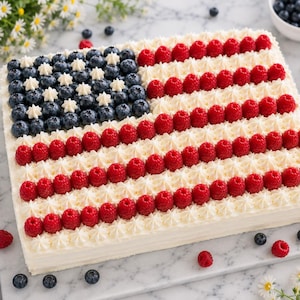 May include: A rectangular sheet cake decorated with white frosting, fresh blueberries, and raspberries arranged to resemble the American flag. The top left corner features blueberries and white frosting stars, while the rest displays stripes of raspberries.