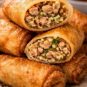 Puede incluir: Primer plano de rollitos de huevo dorados, uno cortado para revelar un relleno sabroso de carne picada, verduras y condimentos. El exterior crujiente contrasta con el interior suave y sabroso. Un delicioso aperitivo o merienda.