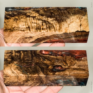 Könnte beinhalten: Zwei rechteckige Holzblöcke mit komplizierten Maserungsmustern und eingebettetem rotem, blauem und schwarzem Harz. Das Holz hat eine warme, natürliche Farbe mit dunkelbraunen und beigen Wirbeln. Die Blöcke werden in Händen gehalten.