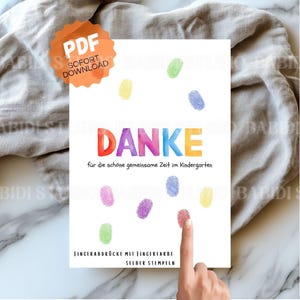Può includere: Una carta bianca con impronte digitali colorate e la parola "DANKE" a colori arcobaleno. Il testo "für die schöne gemeinsame Zeit im Kindergarten" è sotto. La carta dice anche "FINGERABDRÜCKE MIT FINGERFARBE SELBER STEMPELN".