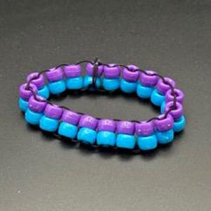 May include: A handmade bracelet featuring alternating rows of turquoise and purple beads. The beads are strung together with black elastic cord, creating a vibrant and colorful accessory. The bracelet is designed to be worn on the wrist.