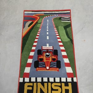 May include: A rectangular rug featuring a race car on a track. The track is gray with white dashed lines, red and white borders, and green grass. The race car is red and yellow. The word "FINISH" is at the bottom.