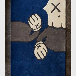 Peut inclure: Un tapis rectangulaire avec un motif de personnage de dessin anim&eacute;. Le tapis pr&eacute;sente un fond bleu avec un motif de personnage gris et blanc cass&eacute;. Le personnage a des mains gant&eacute;es blanches avec des marques "X" noires.
