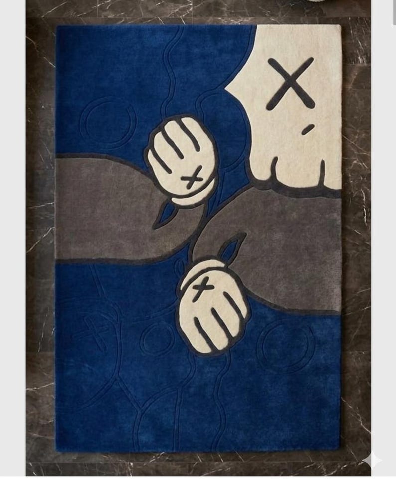 Peut inclure: Un tapis rectangulaire avec un motif de personnage de dessin anim&eacute;. Le tapis pr&eacute;sente un fond bleu avec un motif de personnage gris et blanc cass&eacute;. Le personnage a des mains gant&eacute;es blanches avec des marques "X" noires.