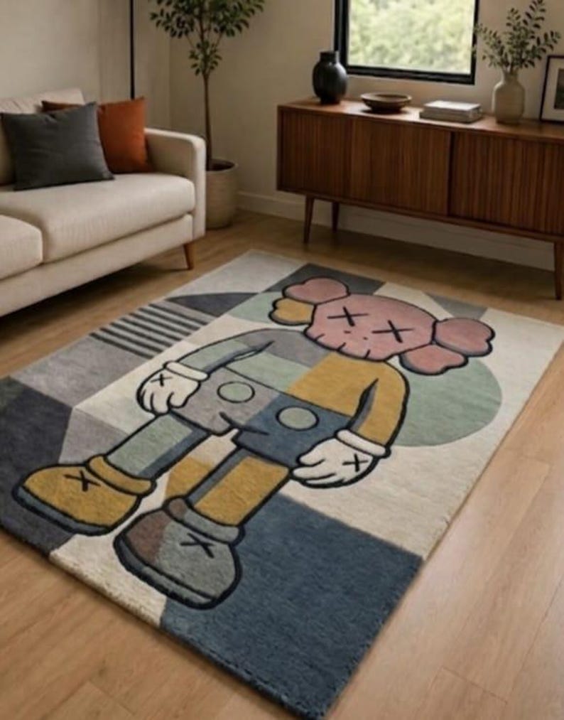 May include: A rectangular rug with a cartoon character design. The rug has a geometric pattern in grey, blue, yellow, and cream. The cartoon character is in the centre, with pink, yellow, and blue colours.