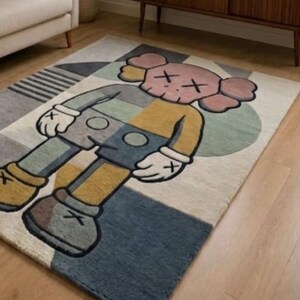 May include: A rectangular rug with a cartoon character design in grey, yellow, blue, and pink. The rug has a geometric pattern and is placed on a wooden floor.