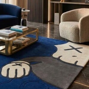 Peut inclure: Tapis moderne avec un motif de personnage de dessin anim&eacute; en bleu, gris et cr&egrave;me. Le tapis est dans un salon avec une table basse dor&eacute;e, un canap&eacute; bleu et un fauteuil beige. Le design du tapis est une caract&eacute;ristique cl&eacute;.