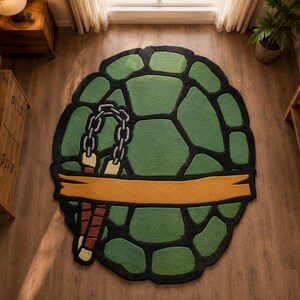 Könnte beinhalten: Ein runder Teppich mit einem grün-schwarzen Schildkrötenpanzermuster. Ein orangefarbenes horizontales Band verläuft durch die Mitte des Teppichs. Ein Paar Nunchakus mit braunen Griffen, gelben Spitzen und einer silbernen Kette ist links abgebildet.